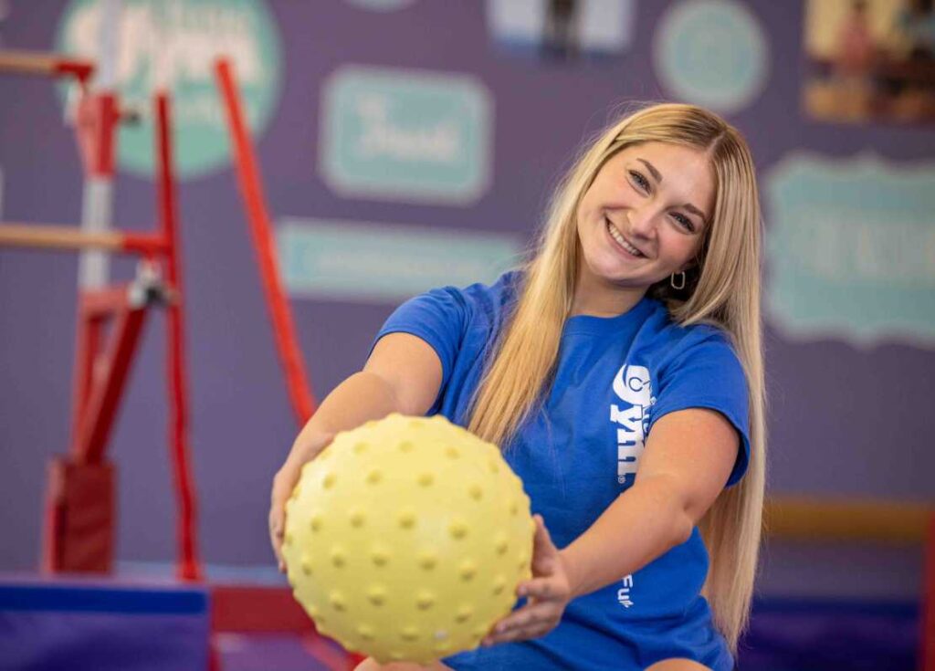 a little gym instructor holding a yellow ball