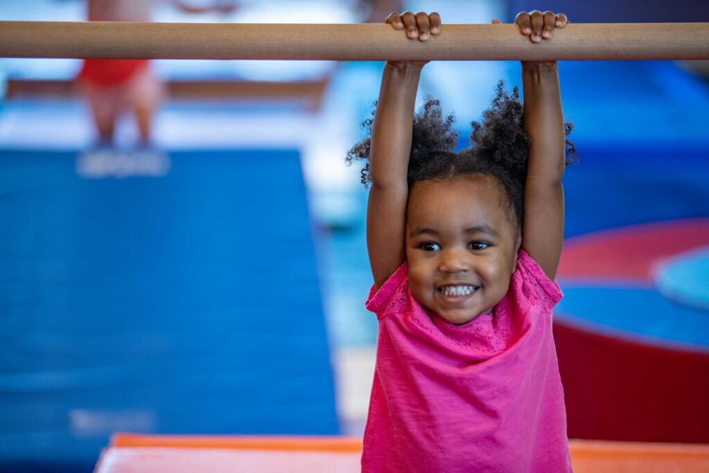 TheLittleGymJan2020-144 young girl hanging from a gymnastics bar