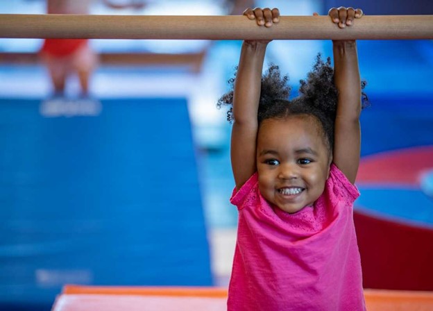Toddler hanging off a gym bar at the Little Gym