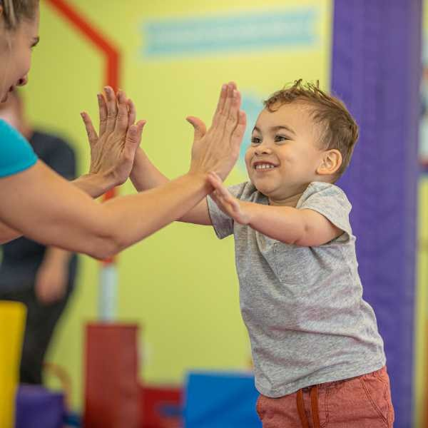 A young child giving a high five to a little gym coach